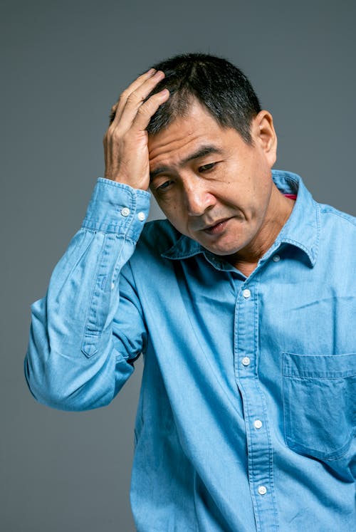 Man in Blue Denim Button Up Long Sleeve Shirt with Hand on His Head