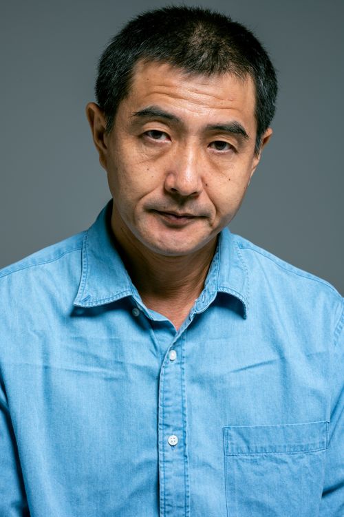 Free A mature Asian man in a blue denim shirt with a serious expression on a neutral background. Stock Photo