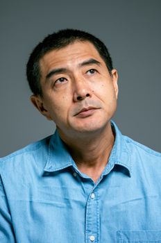 一位成熟亚洲男子的特写肖像，穿着蓝色衬衫，看起来若有所思