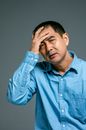 在灰色背景下，一位穿着蓝色衬衫的男人正把手放在头上，若有所思