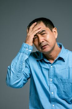 在灰色背景下，一位穿着蓝色衬衫的男人正把手放在头上，若有所思