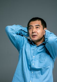 一名穿着蓝色牛仔衬衫的成年男子双手放在头上，在室内看起来若有所思