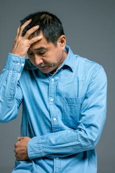 一位身穿蓝色牛仔衬衫的中年男子，手放在头上，表情若有所思