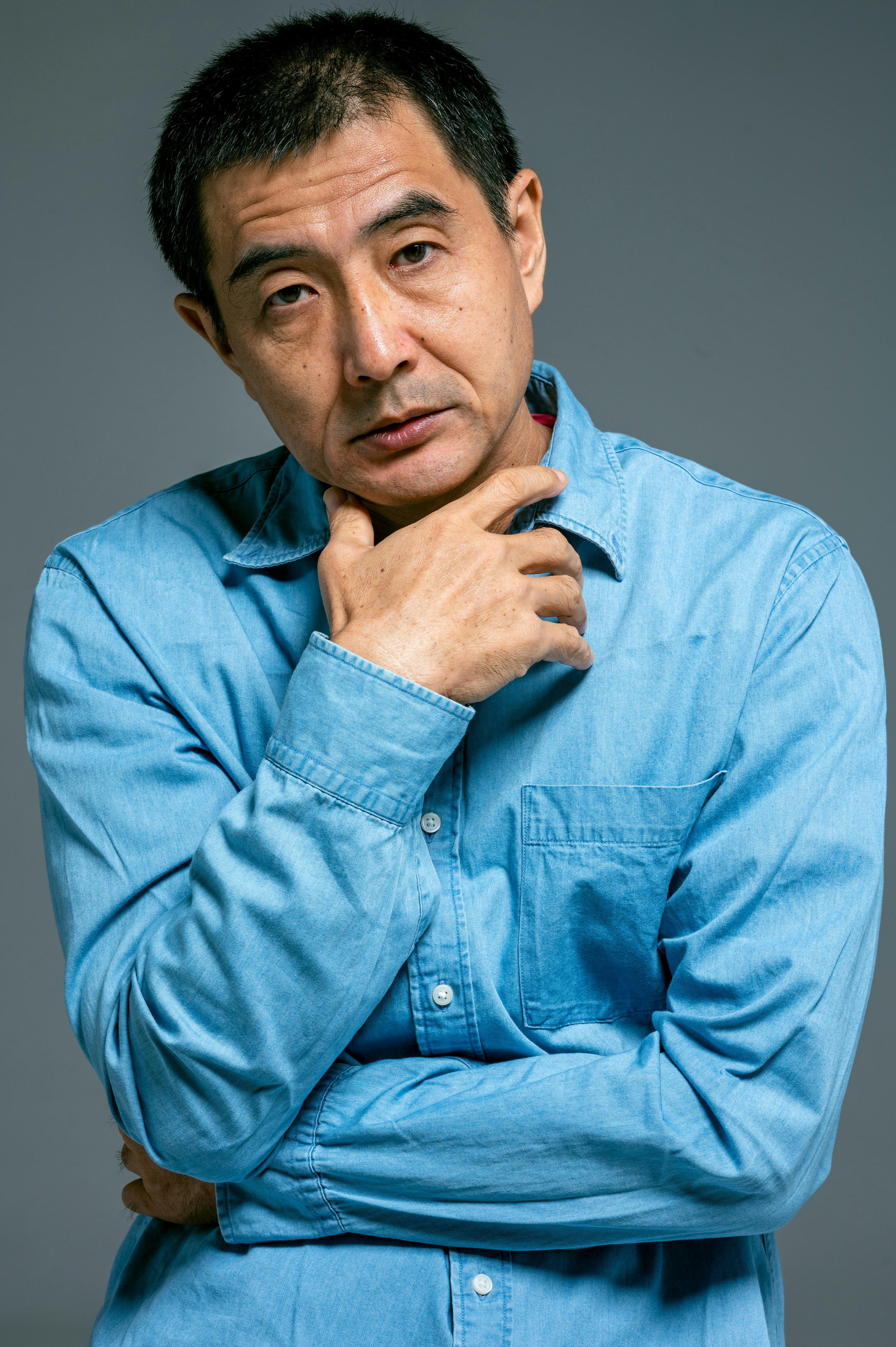 一位穿着蓝色牛仔衬衫的体贴男人，手托下巴，神情严肃