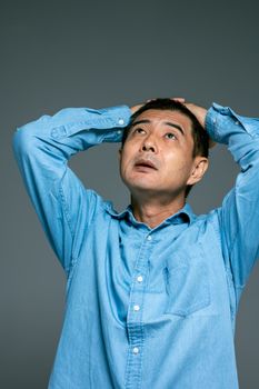 一名穿着蓝色牛仔衬衫的成年男子，双手放在头上，若有所思地向上凝视