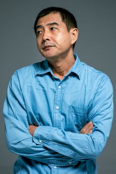 一名身穿蓝色牛仔衬衫的成年亚洲男子双臂交叉，若有所思