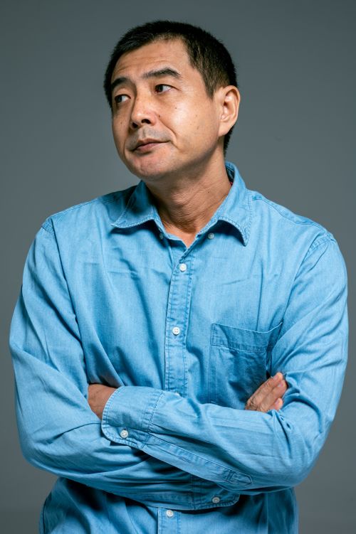 Free An adult Asian man in a blue denim shirt with arms crossed, expressing a thoughtful mood. Stock Photo