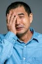 一名身穿蓝色牛仔衬衫的亚洲男子特写镜头中，他用手捂住脸，表达了深深的情感