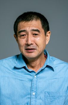 一位穿着蓝色牛仔衬衫的亚洲男子，肖像中流露出焦虑与悲伤