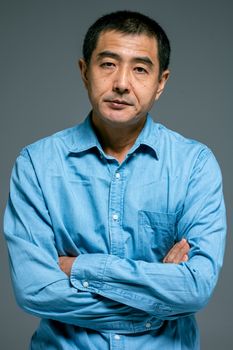 一位表情严肃、双臂交叉、穿着蓝色牛仔衬衫的亚洲中年男子肖像