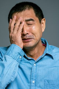 一名身穿蓝色衬衫的男子痛苦地捂住脸，流露出悲伤的特写