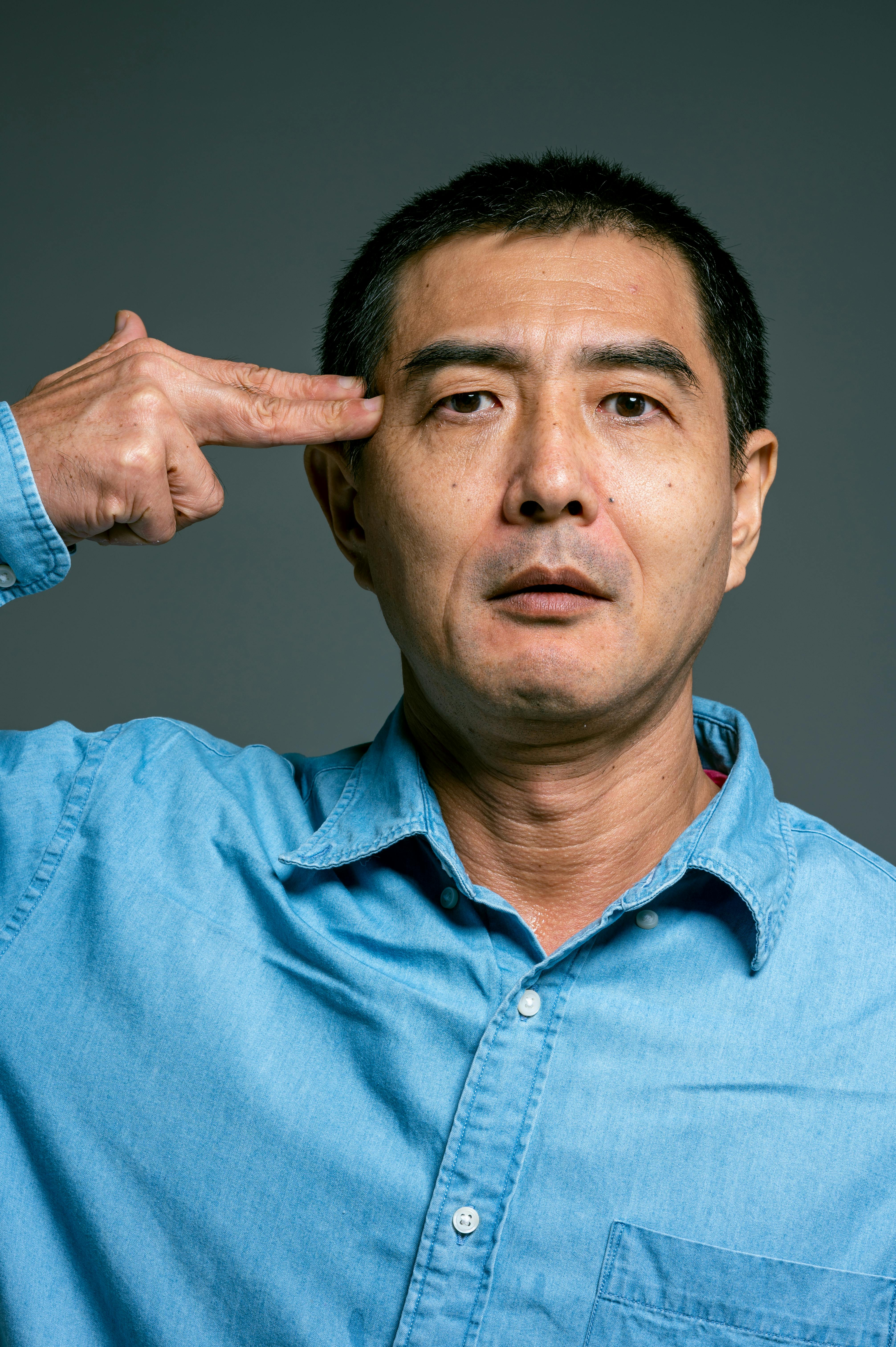 man in blue button up shirt with fingers on head