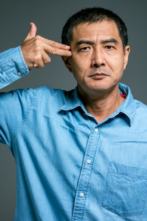 Man in Blue Button Up Shirt Pointing Finger on Face