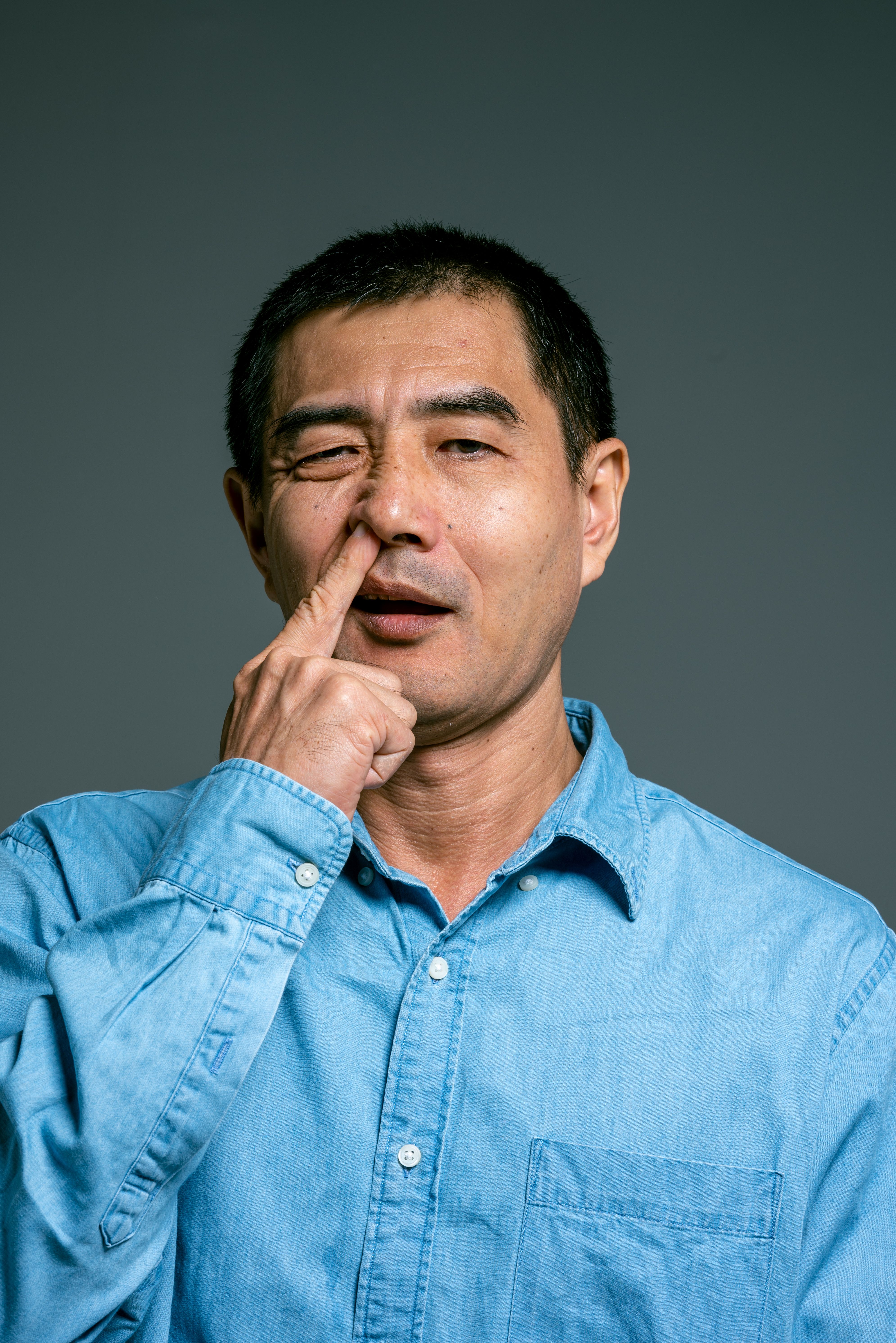 A man in a blue denim shirt making a funny facial expression in a studio setting.