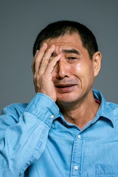 特写镜头中，一名穿着牛仔衬衫的成年男子用手捂着脸，神情悲伤