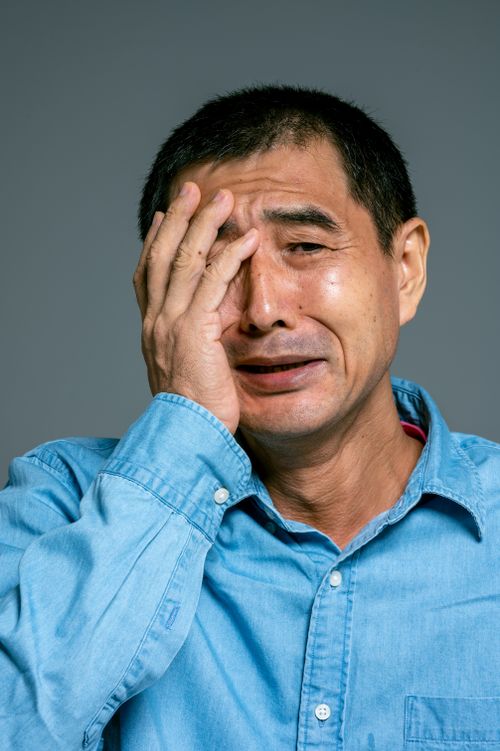 Free Close-up shot of an adult man in a denim shirt expressing sadness with a hand on his face. Stock Photo