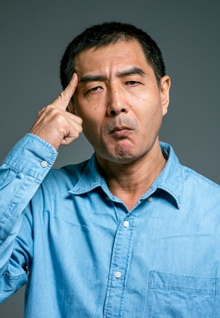 Man In Blue Top Pointing Finger On Forehead