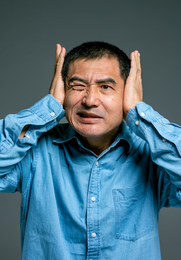 Man In Blue Button Up Shirt Covering Ears With Palm