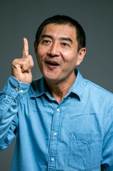 一名穿着蓝色牛仔布的亚洲男子手指向上，表达着一个想法