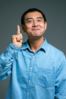 一名穿着蓝色休闲衬衫的男子微笑着向上指去，暗示着一个想法或实现