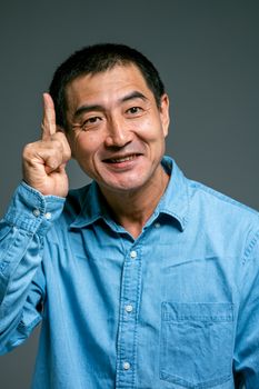 一位穿着蓝色牛仔衬衫的亚洲男子微笑着指向上面，仿佛想到了什么
