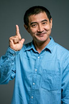 一位身穿蓝色牛仔衬衫的亚洲男子微笑着，手指向上方