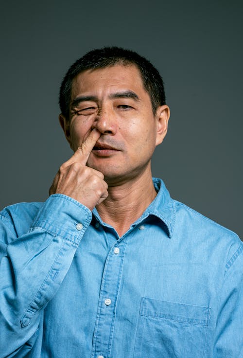 A Man in Blue Denim Button Up Shirt Nose Picking