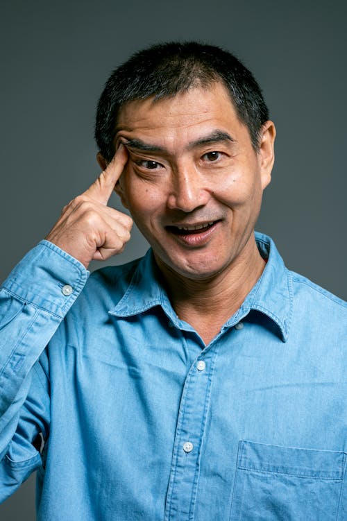 Man in Blue Denim Button Up Shirt Pointing Finger on Eyebrow
