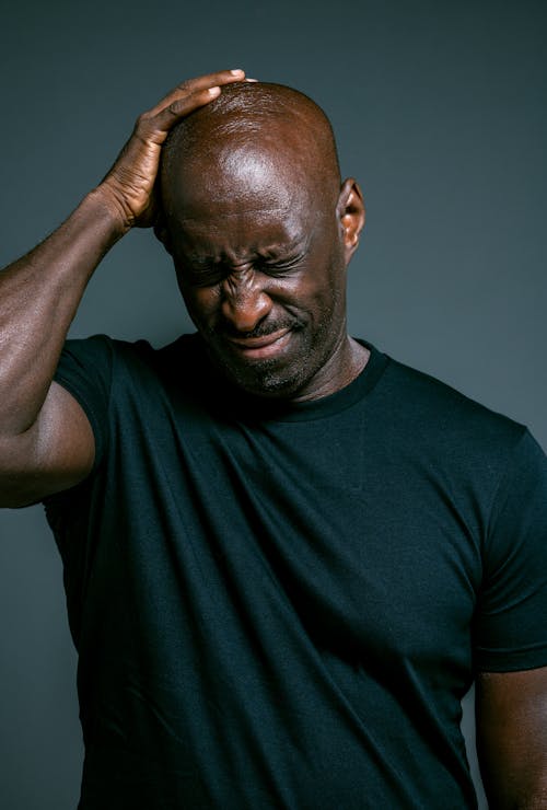 Man in Blue Crew Neck Shirt Holding His Bald Head