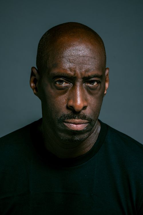 Free Close-up portrait of a serious bald man wearing a black shirt, set against a dark background. Stock Photo