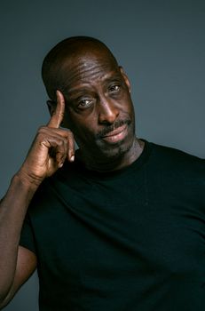 这是一幅特写肖像，描绘了一位穿着深色衬衫、陷入沉思的黑人，他正轻触自己的太阳穴