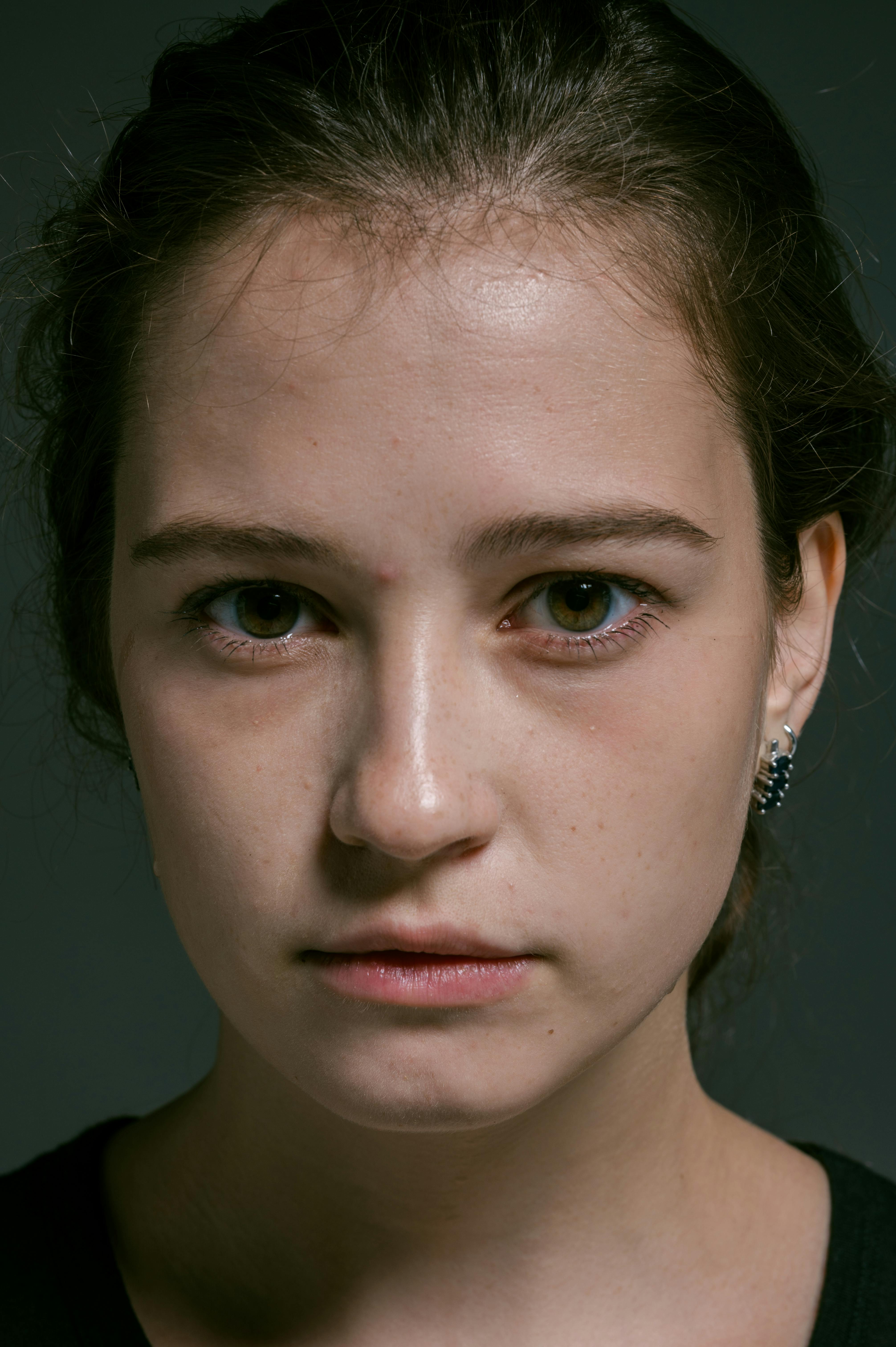 A detailed close-up portrait of a young woman wearing earrings, set against a dark background.