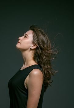 深色背景前，一位身穿黑色无袖上衣、长发飘逸的女性侧影