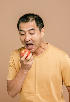 一名男子穿着米色衬衫，兴奋地拿着一个新鲜的红苹果，背景是棕褐色