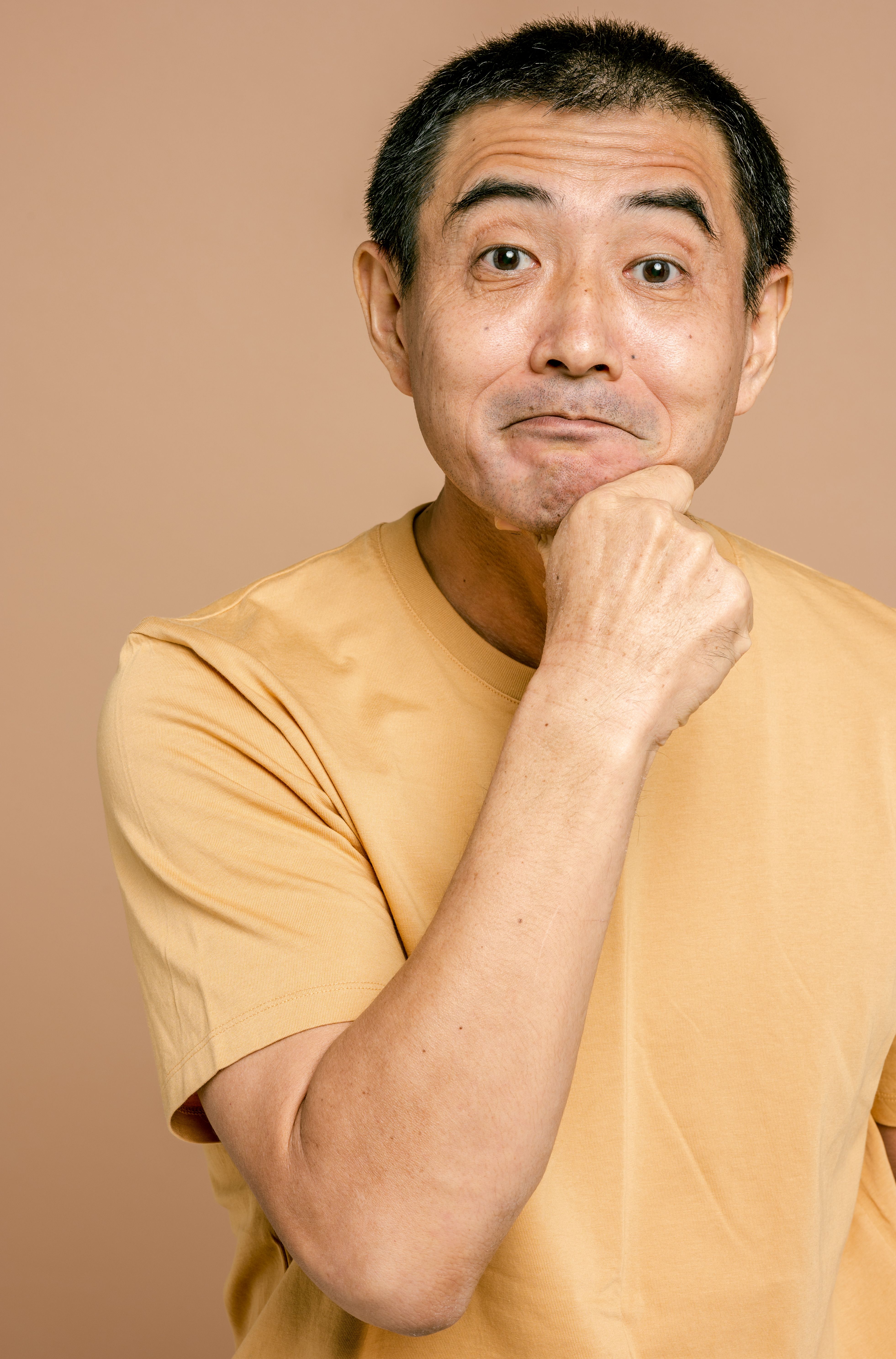 Portrait of a cheerful mature man in a casual t-shirt with hand on chin, smiling warmly.