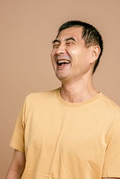 Portrait of a laughing man wearing a yellow t-shirt, expressing happiness against a beige backdrop.