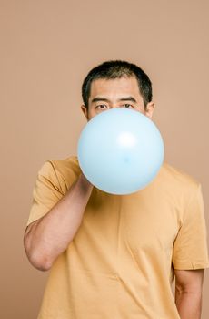 一位老年男子在室内米色背景前给蓝色气球充气