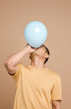 一位穿着休闲服装的成年男子在米色背景下吹着蓝色气球