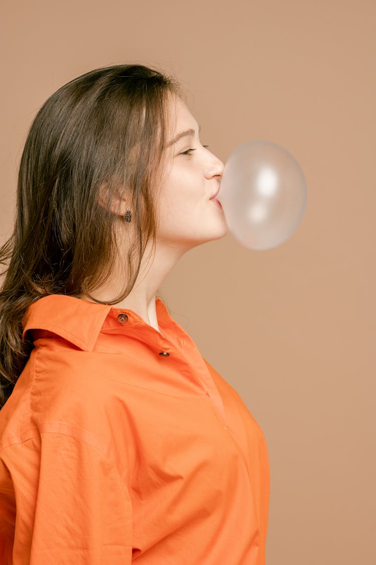 A Woman In Orange Button Up Shirt Blowing A Bubble Gum