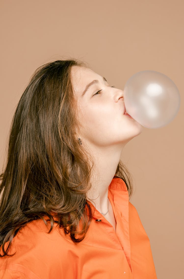 A Woman In Orange Shirt Blowing A Bubble Gum