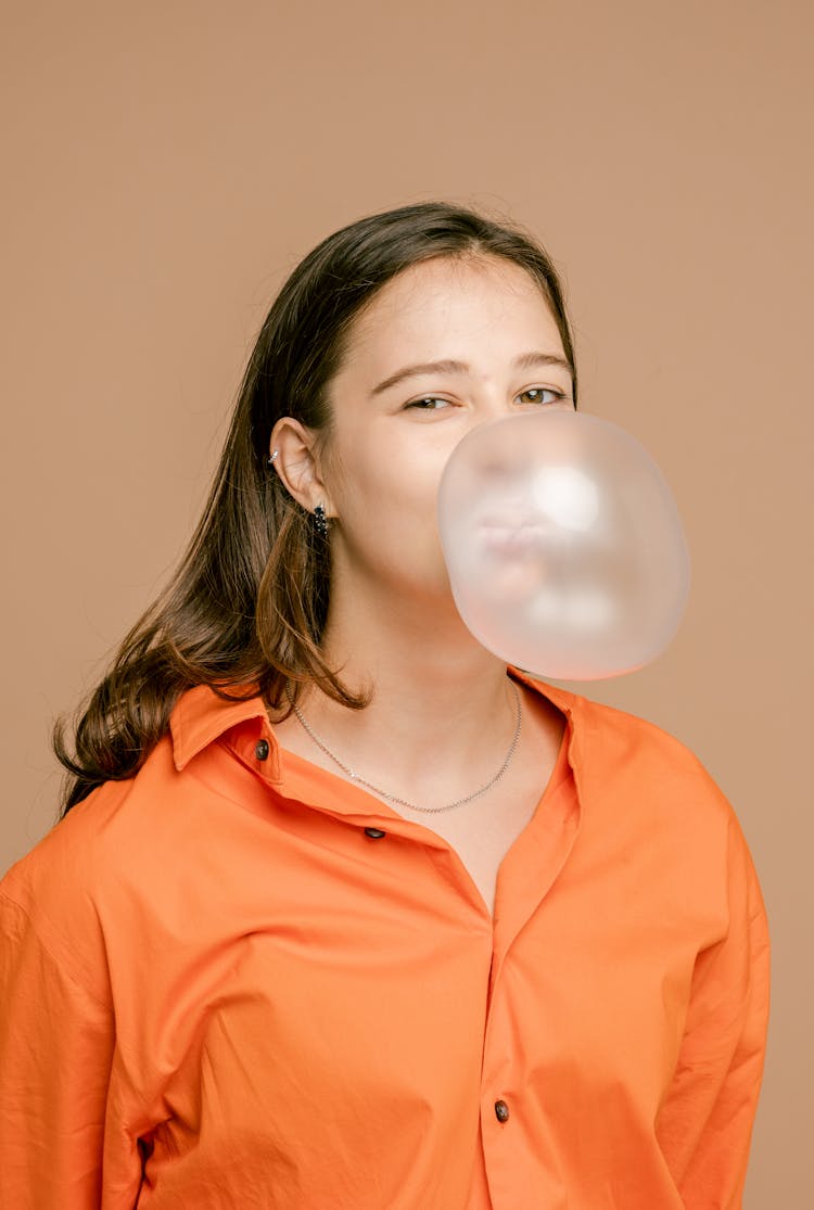 A Woman In Orange Button Up Shirt Blowing A Bubble Gum