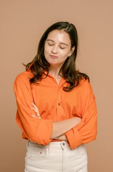 一位年轻女子穿着橙色衬衫，在米色背景前表情俏皮