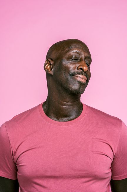 Portrait of a bald man in a pink shirt against a matching background with eyes closed.