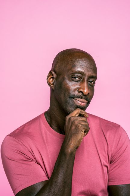 Confident portrait of a man in a pink shirt, posing thoughtfully against a pink background.