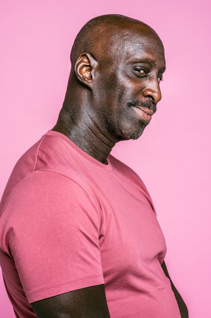 Side profile portrait of a smiling man wearing a pink t-shirt against a pink background.