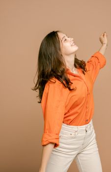 一位开朗的年轻女子穿着时尚的橙色衬衫，在米色背景下快乐地跳舞