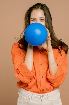 一位穿着橙色衬衫的顽皮年轻女子，正在米色背景下给蓝色气球充气