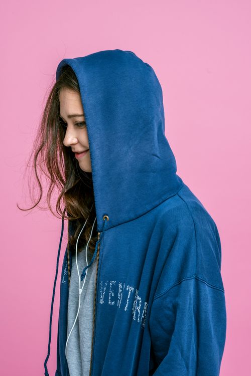 Free Young girl in blue hoodie listening to music, pink background. Stock Photo