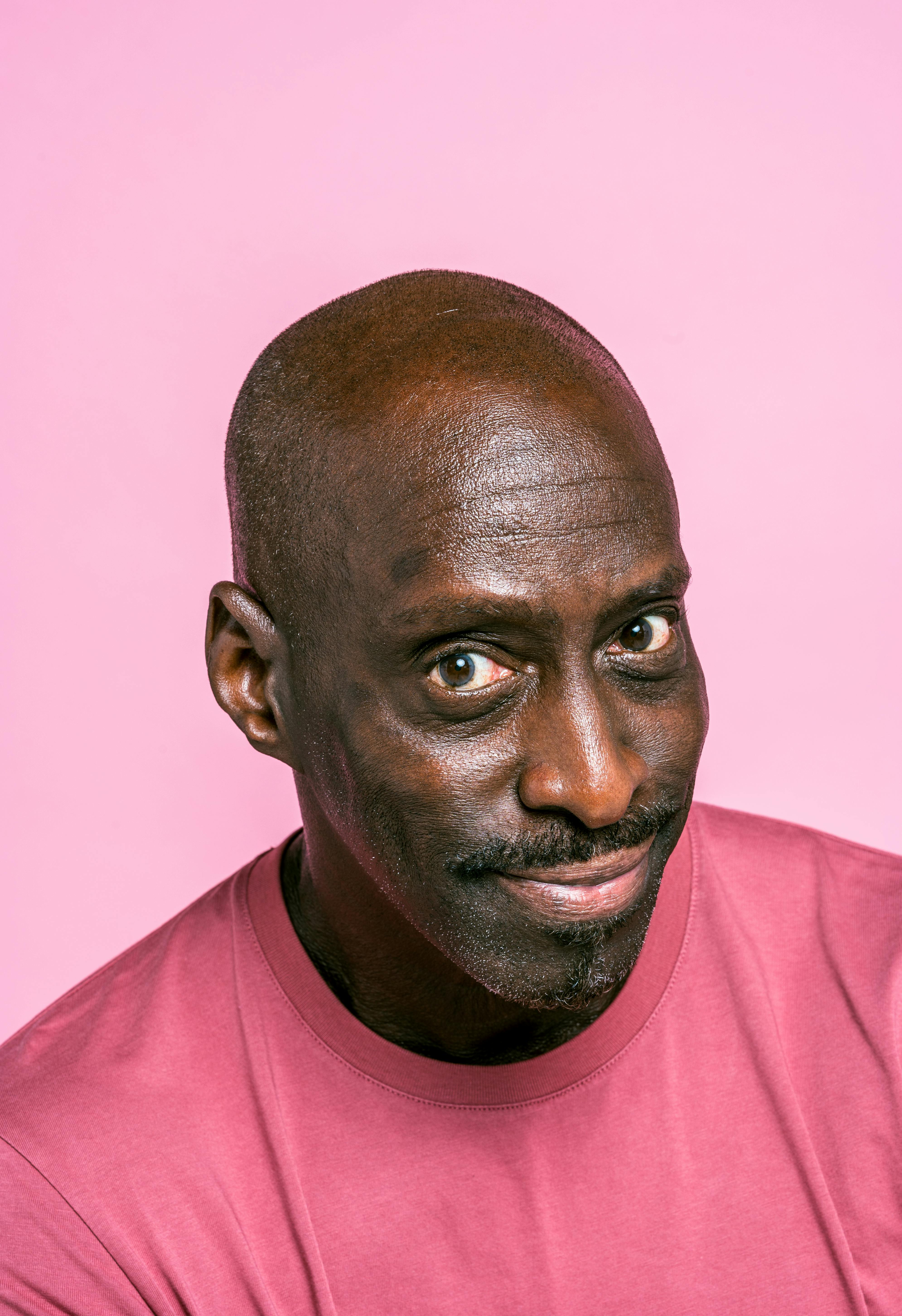 Close-up portrait of a mature black man smiling against a pink background.
