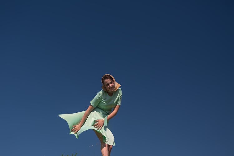 Young Cheerful Lady With Fluttering Skirt On Wind Against Blue Sky